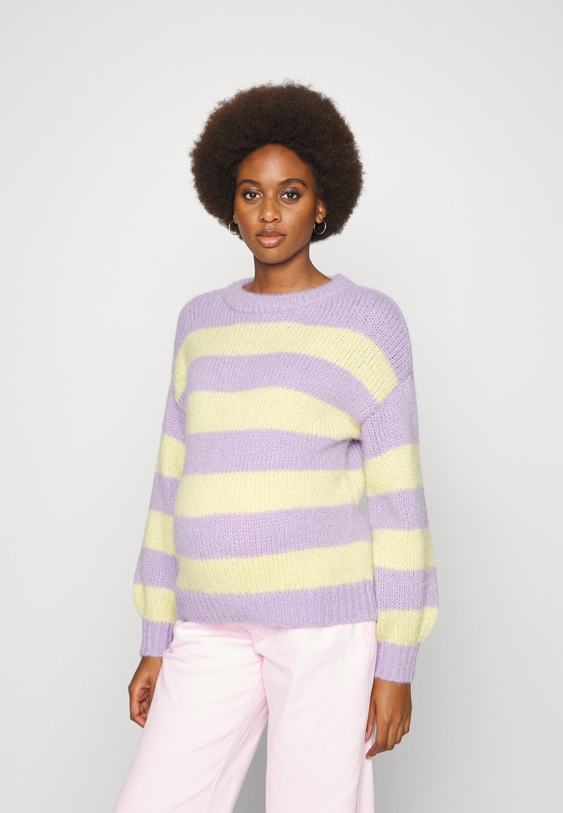 Suéter tricotado em listras lavanda e amarelas. Apresenta um decote redondo e mangas balão. Combinado com calças rosa-claro. Textura suave.