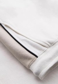 Gros plan d'une manche en tissu blanc et beige avec un poignet côtelé et une fine bordure noire le long de la couture.