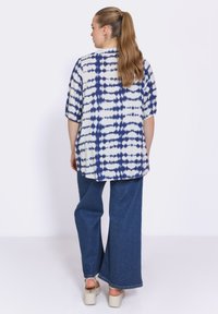 Het shirt heeft een wit en marineblauw tie-dye patroon, met halve mouwen en een losse pasvorm, gecombineerd met wijde denimbroeken en sleehakken.