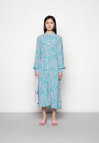 Vestido longo abotoado em verde-água claro com padrões abstratos em rosa, mangas franzidas e um corte reto. Combinado com sapatos de salto bloco rosa e uma bolsa lavanda.