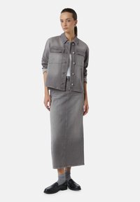 Grijze denim jas met twee borstzakken, gecombineerd met een bijpassende lange rok. Zwarte schoenen en grijze ribbelkousen maken de outfit compleet.