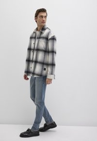 Black and white plaid flannel shirt with button closure, worn over a light-colored top, paired with blue jeans and black shoes.