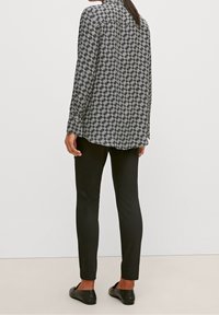 Chemise à manches longues en tissu à motifs noir et blanc, dotée d'un col montant et d'une coupe légèrement ample, associée à un pantalon noir ajusté.