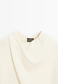 Gros plan sur un pull en laine couleur crème à col rond avec une étiquette noire Massimo Dutti visible à l'intérieur du col.
