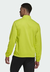 Fluoreszierend gelbe Langarmjacke mit hohem Kragen, glatter Textur und schmal zulaufenden Bündchen, kombiniert mit schwarzen Hosen.