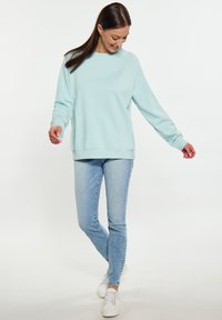 Felpa azzurra chiara realizzata in un materiale morbido, con colletto rotondo e polsini a coste, abbinata a jeans slim fit in denim chiaro e sneakers bianche.