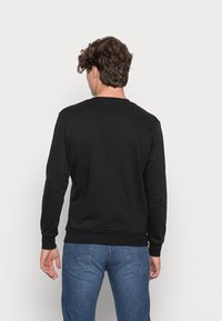 Sudadera negra de manga larga con cuello redondo, puños y dobladillo acanalados; combinada con vaqueros azules, vista desde atrás. Textura suave.