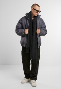 Grå puffjacka med texturerad yta, i kombination med en svart scarf och svarta cargobyxor, kompletterad med vita sneakers.