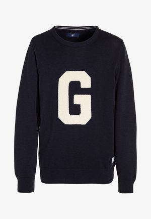 Pull tricoté bleu marine avec un grand écusson "G" crème sur le devant. Encolure et poignets côtelés, avec une étiquette sur le côté inférieur.