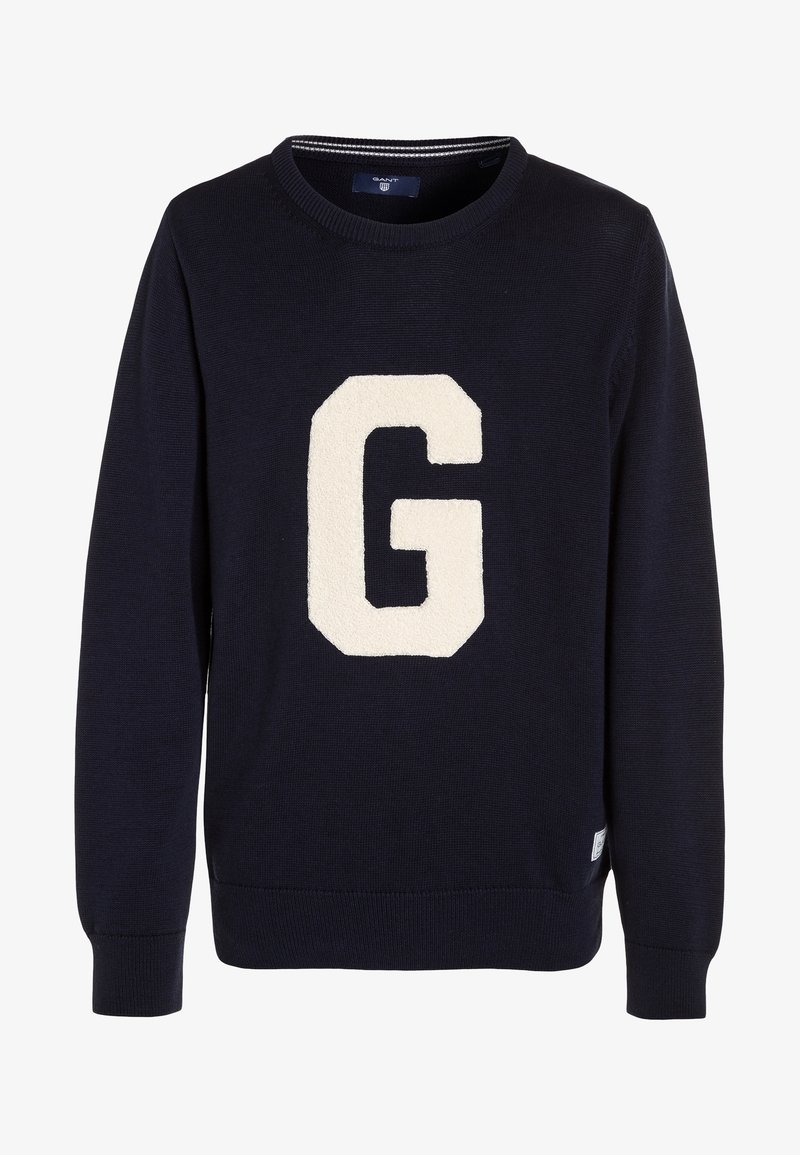 Pull tricoté bleu marine avec un grand écusson "G" crème sur le devant. Encolure et poignets côtelés, avec une étiquette sur le côté inférieur.