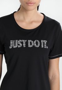 Svart kortärmad T-shirt med en silverglittrande tryckt slogan "JUST DO IT." och kontrasterande sömmar vid halsringningen och ärmarna.
