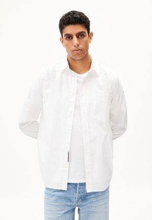 White collared shirt, made of cotton, with a chest pocket and button closure, worn over a white t-shirt, paired with light blue denim jeans.
