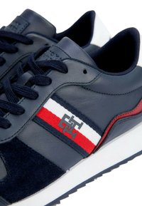 Sneakers in pelle blu navy con sovrapposizione in camoscio, striscia bianca e rossa e un logo a contrasto sul lato. Suola bianca.