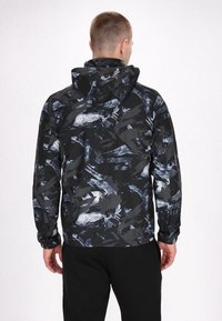 Veste noire à capuche arborant un motif abstrait dynamique en nuances de bleu et de gris, confectionnée dans un tissu léger avec des poignets élastiques.