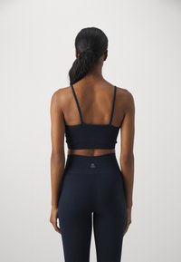 Top court côtelé bleu marine avec des fines bretelles, associé à des leggings côtelés taille haute comportant un petit logo sur la ceinture.