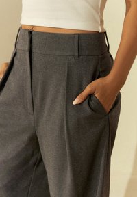 Pantaloni grigi su misura con una texture liscia, dotati di tasche laterali e design frontale piatto. Realizzati in un materiale tessuto.