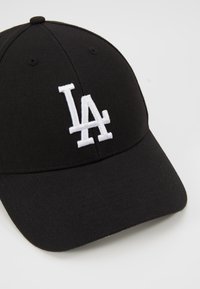 Svart baseballcaps laget av stoff, med en hvit brodert "LA"-logo på fronten og en buet skjerm. Teksturert stoff og justerbar passform.