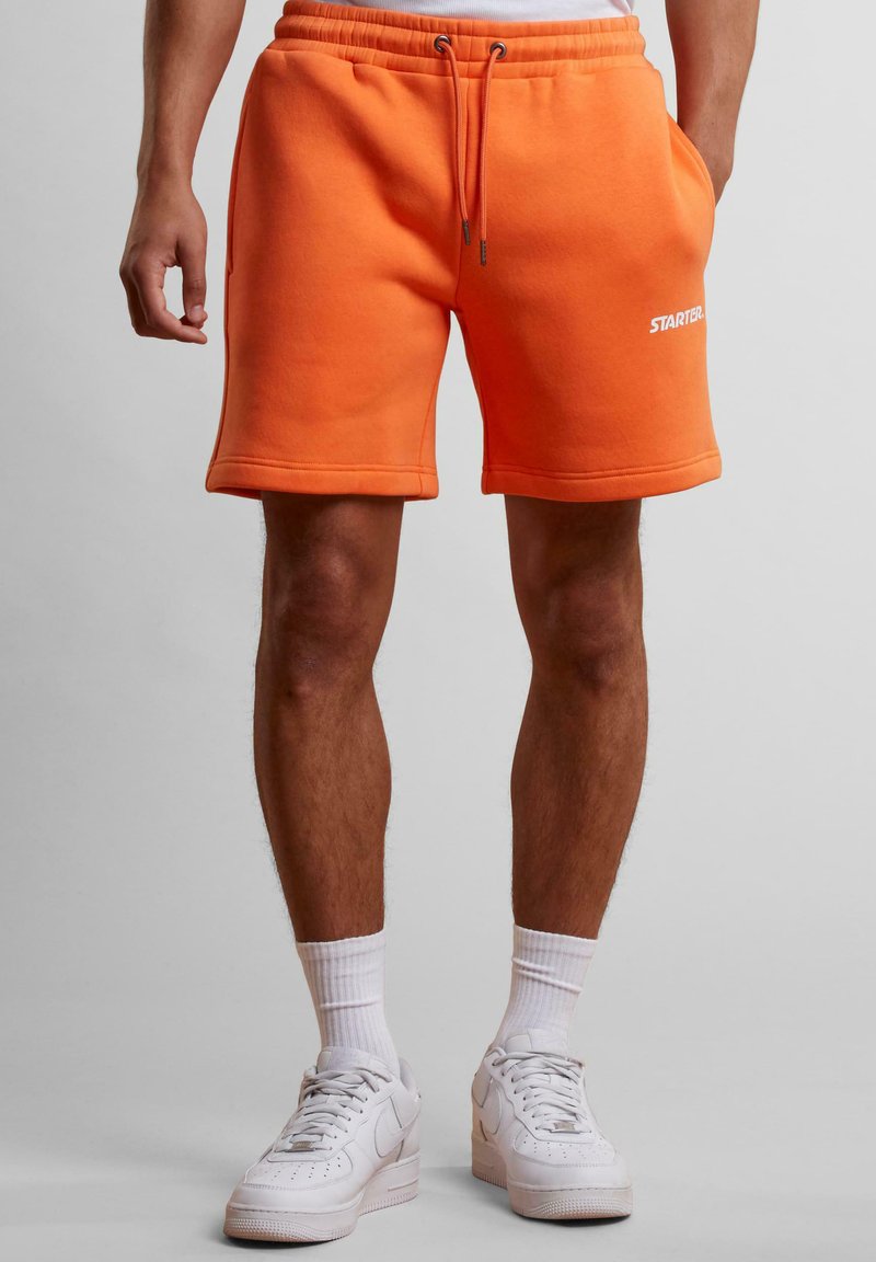Shorts en polaire orange avec une taille élastique et un cordon de serrage. Comprend des poches latérales et un logo « STARTER » blanc au bas.