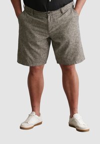 Gemusterte Shorts in gedämpften Grautönen, mit lockerer Passform, seitlichen Taschen und einem Knopfverschluss, getragen mit weißen Sneakern.