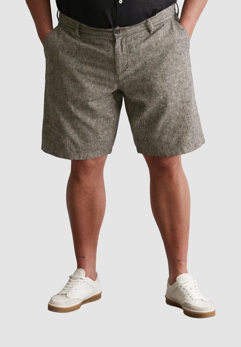 Gemusterte Shorts in gedämpften Grautönen, mit lockerer Passform, seitlichen Taschen und einem Knopfverschluss, getragen mit weißen Sneakern.