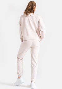 Jasnoróżowa bluzka z kapturem i pasujące dresy, wykonane z miękkiego materiału. Charakteryzują się luźnym krojem, prążkowanymi mankietami i białymi trampkami. Prosty design.