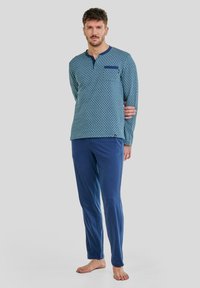 Conjunto de pijama para hombre; parte superior de manga larga en turquesa con un patrón geométrico, pantalones azules, tejido suave y un bolsillo en el pecho.