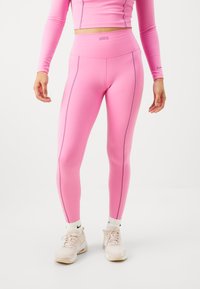 Leggings roses avec taille haute, fabriqués en matière extensible. Présente des coutures contrastantes et un petit logo Nike au niveau de la taille.