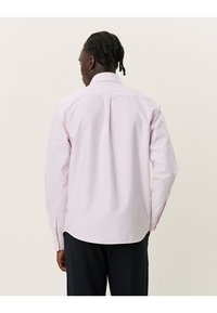 Ljusrosa långärmad skjorta med standardkrage, knäppningar vid ärmsluten och rak veck bak; tillverkad av slätt bomullstyg.