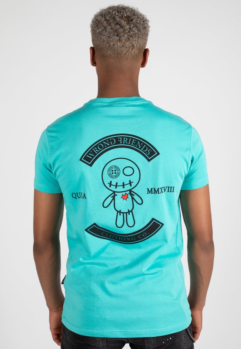 Türkises Baumwoll-T-Shirt mit einem schwarzen Grafikdesign auf der Rückseite, das ein Puppendesign, den Text "FALSCHE FREUNDE" und kreisförmige Akzente zeigt.