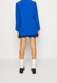 Blå strukturerad kavaj med långa ärmar, i kombination med denimshorts, vita strumpor och svarta plattformsskor. Slät tygtextur, skräddarsydd passform.