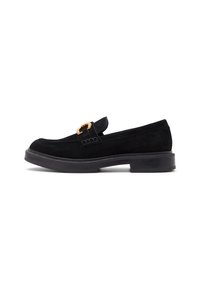 Mocassin en daim noir avec une semelle épaisse et une boucle décorative dorée sur le dessus, vu de côté extérieur sur fond blanc.