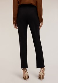Pantalons noirs ajustés avec une texture lisse et une coupe droite, assortis à des sandales à talons hauts nude. L'ensemble est complété par un blouse marron.