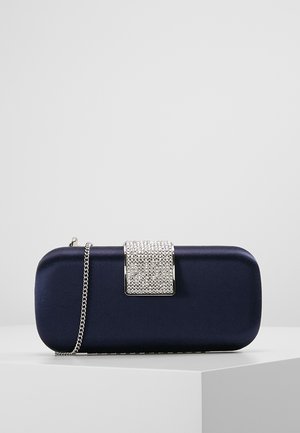 Granatowa prostokątna kopertówka z zapięciem wysadzanym srebrnymi kryształami oraz srebrnym łańcuszkiem, umieszczona na białej powierzchni.