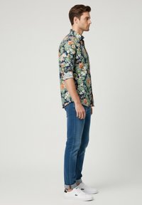 Camisa de botones con patrón floral en azul marino, con flores blancas y naranjas. Combinada con jeans azules arremangados y zapatillas blancas.