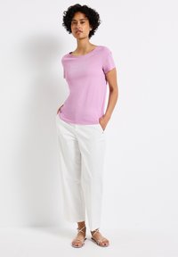 T-shirt rose clair à manches courtes avec un décolleté large et un motif texturé subtil. Associé à un pantalon large blanc et des sandales à lanières.
