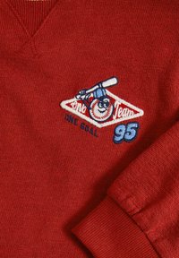 Rode katoenen sweatshirt met een V-hals, geribbelde manchetten en een blauw-witte geborduurde honkbalgrafiek met de tekst "One Goal" en "95."
