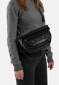 Zwarte leren schoudertas met een voorvak, metalen accenten en een kettingstrap. Het heeft een gladde textuur en een gebogen vorm.
