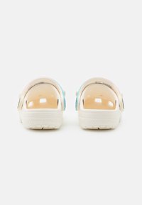 Transparente, rückenfreie Clogs in Creme mit einem mehrfarbigen Farbverlauf. Sie verfügen über abgerundete Kanten und eine strukturierte Sohle mit kleinen Rillenmustern.