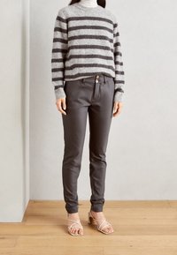 Gray and black striped knit sweater, relaxed fit. Gray, tailored pants with two buttons at the waist. Strappy beige heels, wooden floor background.