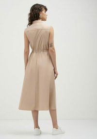 Abito beige senza maniche con colletto, fascia elastica in vita e gonna fluida; realizzato in tessuto leggero. Abbinato a sneaker bianche.