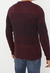Sweter dzianinowy w kolorze burgundowym z ciemnymi poziomymi paskami. Posiada ściągacz przy dekolcie i u dołu, długie rękawy oraz fakturowany materiał.
