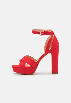 Red suede platform sandals with a wide strap design, ankle buckle, and high block heel, featuring a smooth texture and rounded toe.