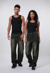 Black sleeveless tops with loose, dark green distressed jeans featuring a star pattern and frayed edges. Black shoes complete the look.