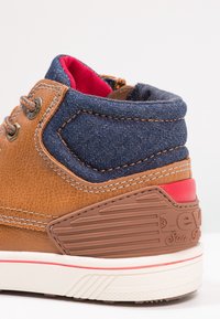 Hnědé kožené a námořnické džíny boty s červeným interiérem, texturovanými akcenty a gumovou podrážkou s tvarovaným logem na patě.