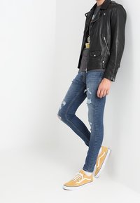 Svart läderbikerjacka, grå grafisk t-shirt, slitna blå skinny jeans och gula sneakers med vita sulor och snören.