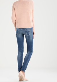 Maglione lavorato a maglia di un delicato colore rosa abbinato a jeans aderenti blu. I jeans presentano un design strappato e sono completati da tacchi alti beige.