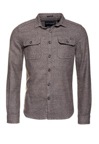 Camisa de manga larga y cuello en tejido gris texturizado. Cuenta con dos bolsillos en el pecho con solapas, botones negros y una etiqueta de marca en el cuello.