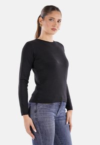 Top nero a maniche lunghe con scollatura rotonda, realizzato in tessuto liscio. Abbinato a jeans blu, che mostrano un design aderente.