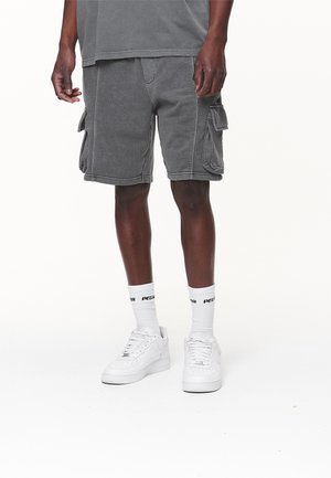 Pantaloncini cargo grigi con più tasche laterali, realizzati in tessuto resistente, abbinati a scarpe bianche e calzini bianchi con logo.