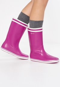 Lila gummistövlar med vita ränder upptill, med en logotyp på utsidan och en texturerad sula för bra grepp.
